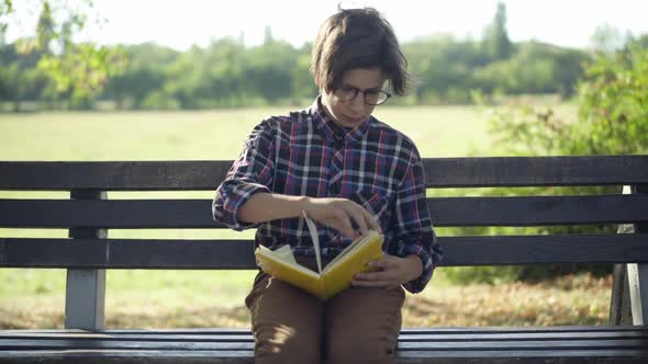 Absorbed Concentrated Smart Teenage Boy Reading Book Sitting in Summer Park Outdoors