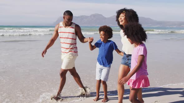 Smiling african american parents and their children walking and holding hands on the beach