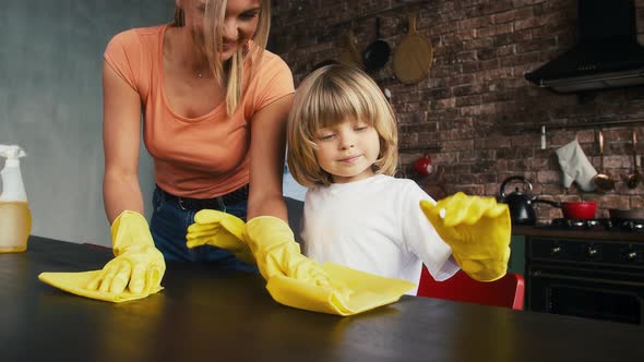 Mommy and Son in Yellow Rubber Gloves are Smiling Talking Scrubbing Table By Rags Using Cleanser at