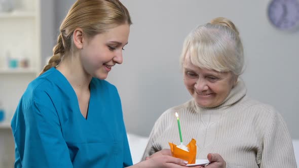 Smiling Medical Worker Bringing Muffin With Candle to Happy Senior Woman, B-Day