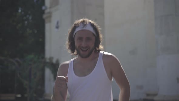 Handsome Positive Young Sportsman Walking Fast in Sunlight Outdoors. Smiling and Winking at Camera