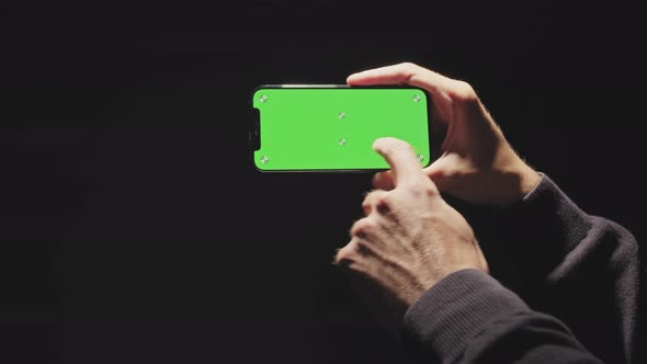 Hand Holds a Black Phone with a Green Screen