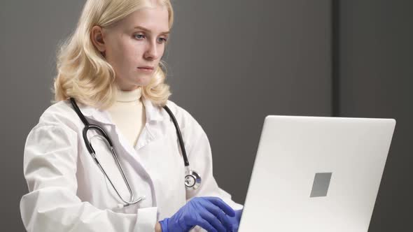 Woman Doctor Working at Computer Entering Data From Patient File