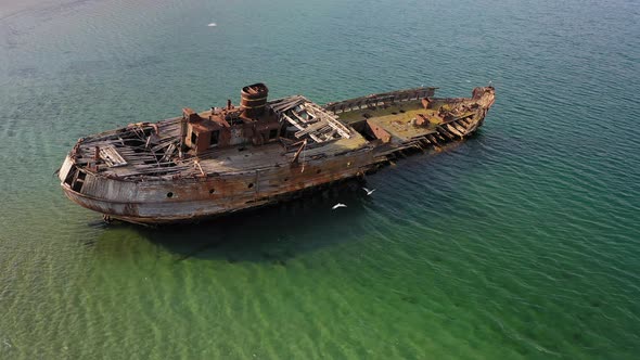 A Wrecked Wooden Ship Lies on the Seashore Covered with Rust