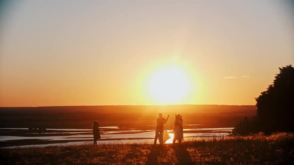 Young Happy Family Playing with a Kite on the Field While the Bright Orange Sunset