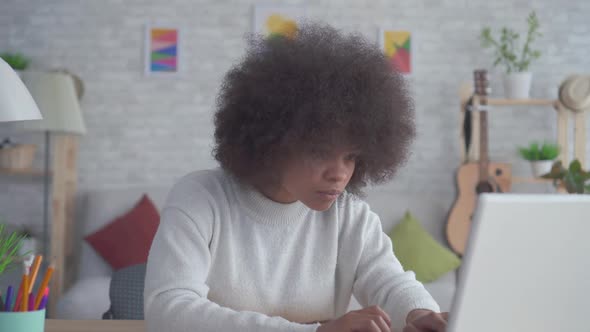 Portrait African American Woman with an Afro Hairstyle Uses a Laptop at Home