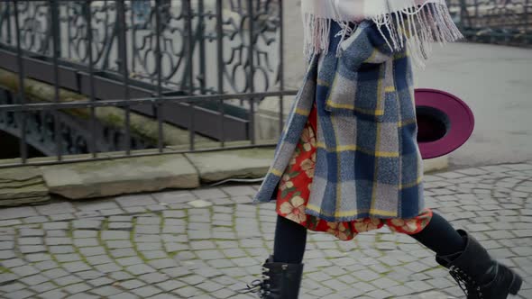 Careless traveler passing a street wearing coat and holding hat in her hand.