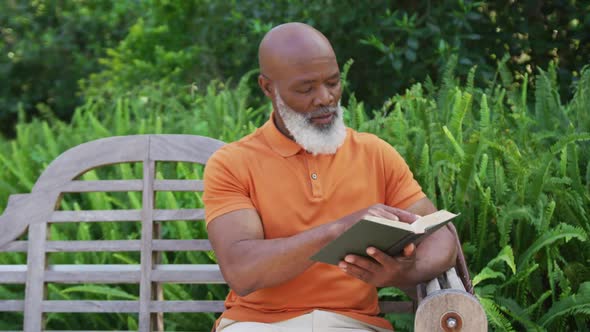 African american senior man reading a book while sitting on a bench in the garden