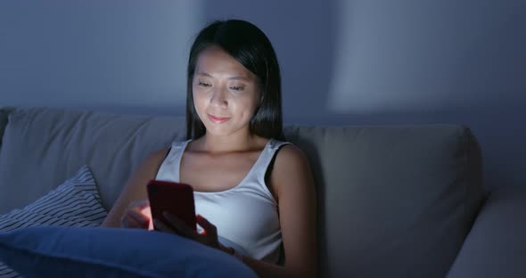 Woman use of smart phone and sit on sofa at home in the evening