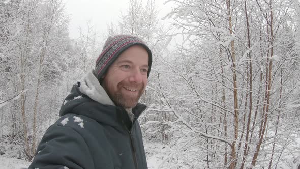 A very happy, ecstatic man in his 30s walks through an idyllic snowy young woodland