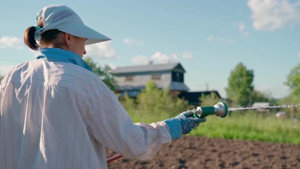 Woman Holding a Water Hose and Watering Beds or Plants in the Backyard