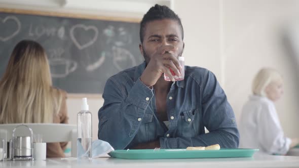 Portrait of African American Man Sitting in Lunchroom with Tray and Drinking Juice