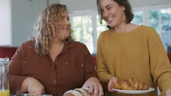 Happy caucasian lesbian couple slicing bread and preparing food in kitchen