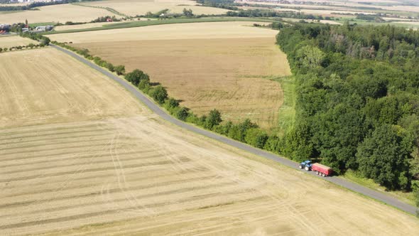 Aerial Drone Shot  a Tractor Drives Down a Road in a Rural Area