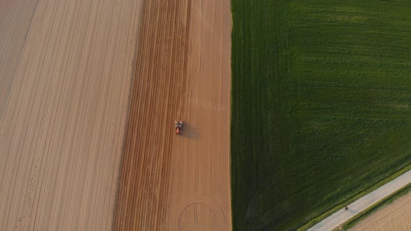Aerial view: tractor working on cultivated fields, farmland by the mountains, agriculture occupation
