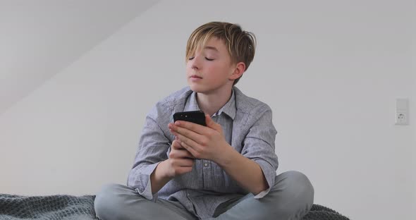 Boy using smartphone sitting on bed at home