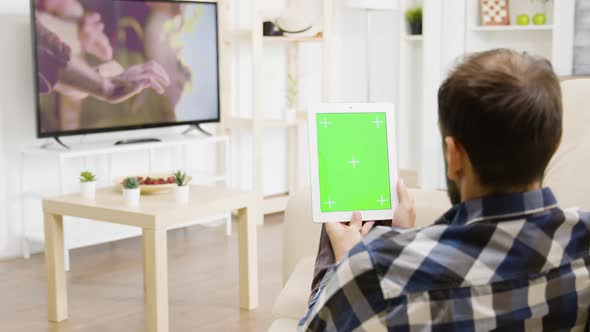 Man Looking at a Movie on the TV While Holding a Green Screen Digital Tablet PC