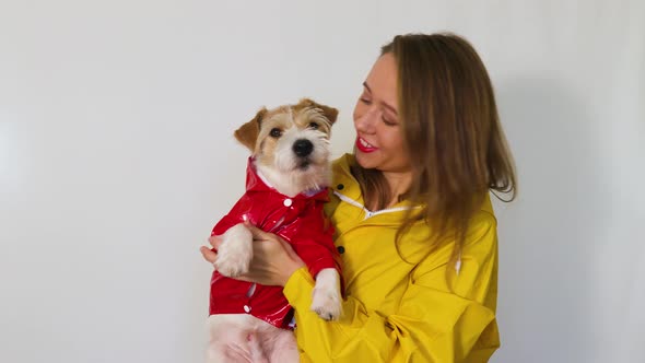 A girl in a yellow raincoat holds a Jack Russell Terrier dog in her hands.