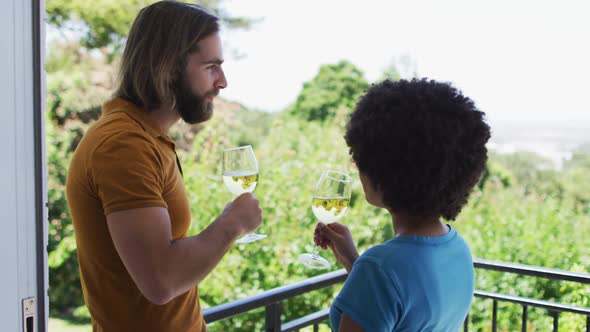 Mixed race couple drinking wine together while standing in the balcony at home