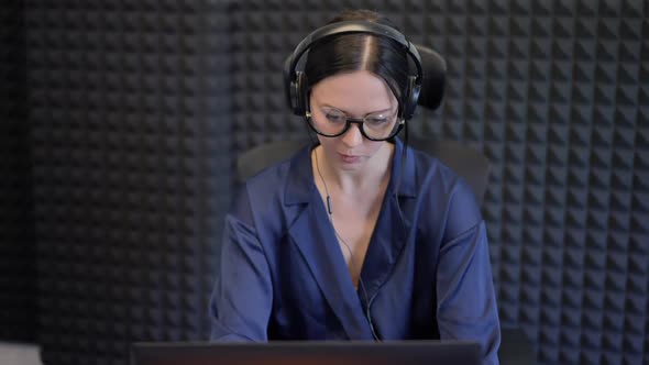 Front View Portrait Young Slim Caucasian Woman in Eyeglasses and Headphones Typing on Laptop
