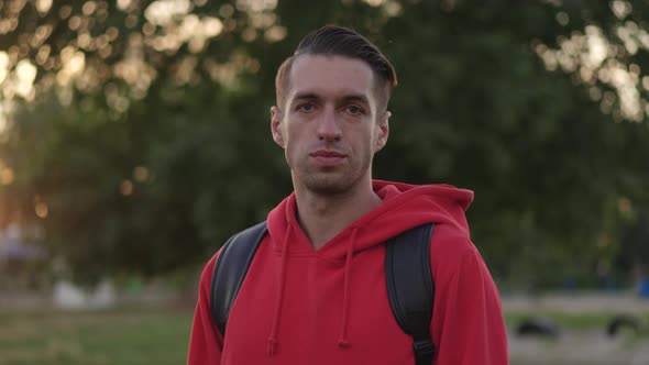 Portrait of Young Male Hipster with a Red Hoodie with a Backpack in a Park at Sunset Background