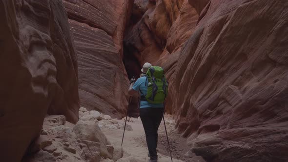 Tourist Hiking In Sandy Riverbed Of Deep Slot Canyon With Orange Rocks Formation