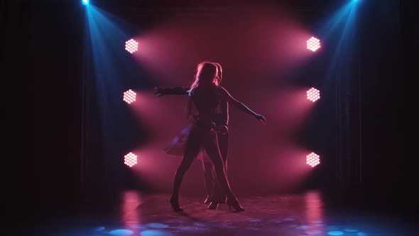 Man and Woman Dancing Rumba in a Dark Studio with Smoke and Stage Light. Silhouettes. Slow Motion.