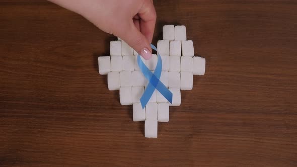 Refined Sugar Cubes in the Shape of a Heart on a Wooden Table with a Blue Ribbon