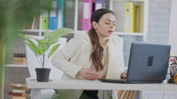 Young Caucasian Woman Sitting in Office at Laptop Having Back Pain