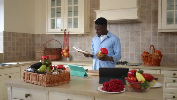 Young Confident African American Man Standing in Kitchen Reading Recipe Holding Conserved Vegetables