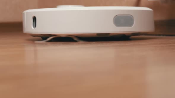 White Robotic Vacuum Cleaner Removes Debris From the Laminate