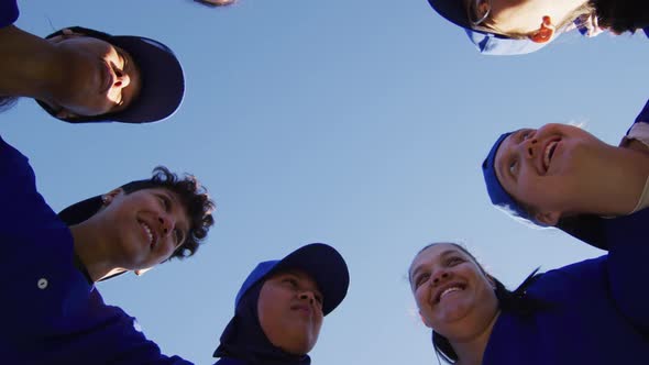 Low angle view of diverse group of female baseball players in a huddle against blue sky