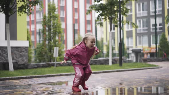 Joyful Blond Little Girl Stomping in Puddle and Running Away. Portrait of Cheerful Cute Caucasian