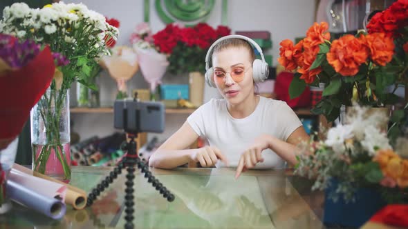 Florist Female in Headphones Communicates with Audience By Video Call Using a Smartphone Girl