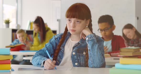 Cute Redhead Preteen Girl in Classroom Writing in Notebook