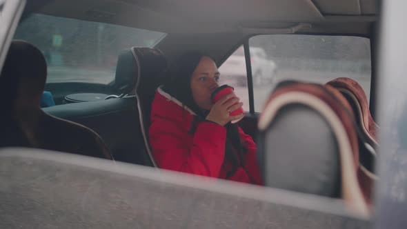 Woman with coffee in car looking out from window