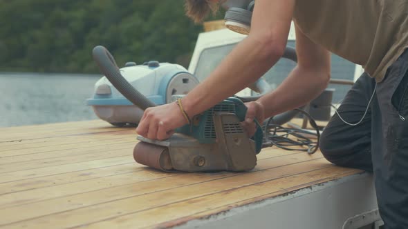 Carpenter using belt sander to sand roof planks of wooden boat roof