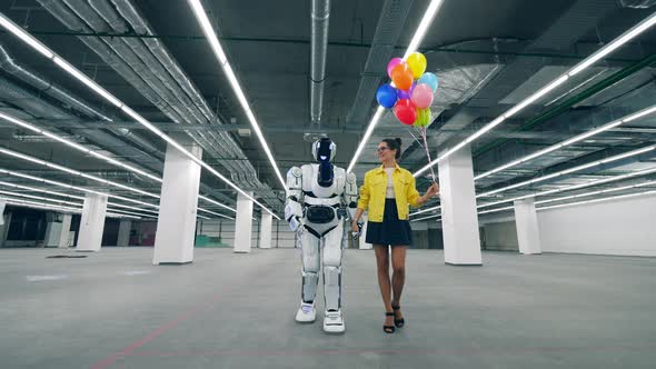 A Lady with Balloons Is Walking with a Cyborg Along the Hall