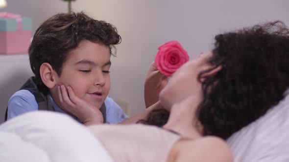 Boy Caressing Sleeping Mom's Face with Rose