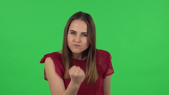 Portrait of Tender Girl in Red Dress Is Threatening with a Fist. Green Screen