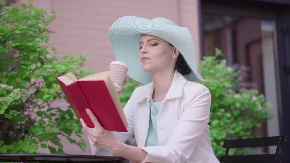 Confident Woman Reading Book and Drinking Coffee in Outdoor Cafe on Summer Day. Portrait of Elegant