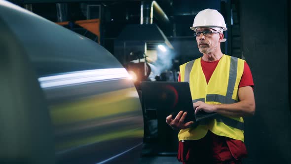 Worker with Laptop Looking at Steel Coil Wrap