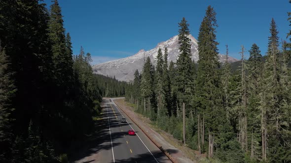 Aerial crane drone shot following cars driving on scenic road toward mountain peak. 