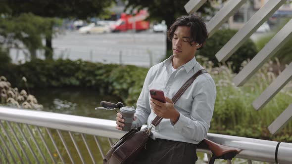 Asian Man Drinking Coffee and Using Mobile on Street