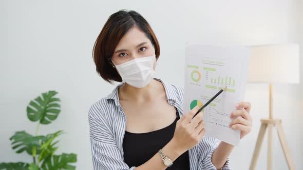 Asian business woman wear face mask presentation to colleague about plan in video call in office.