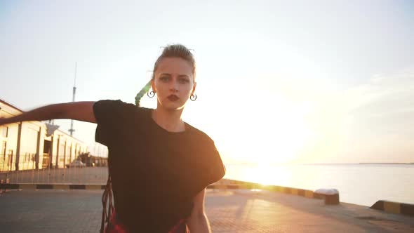 Young Stylish Funky Girl with Green Hair Riding Roller Skates and Dancing Near Sea Port During