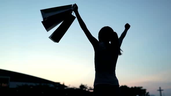 Slow motion of woman raising up shopping bag under sunset 
