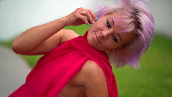 Portrait of a Pretty Girl in a Red Dress and Pink Short Hair on a Walk in the Park