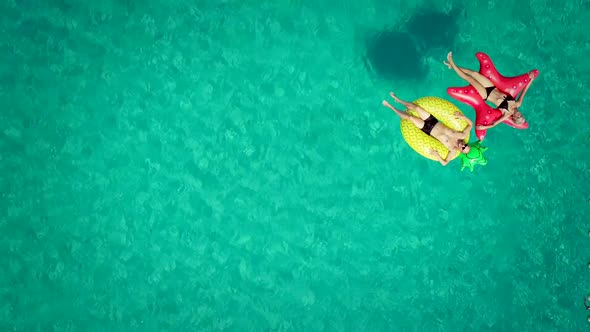 Aerial view of man and woman floating by string buoy on inflatable mattresses.