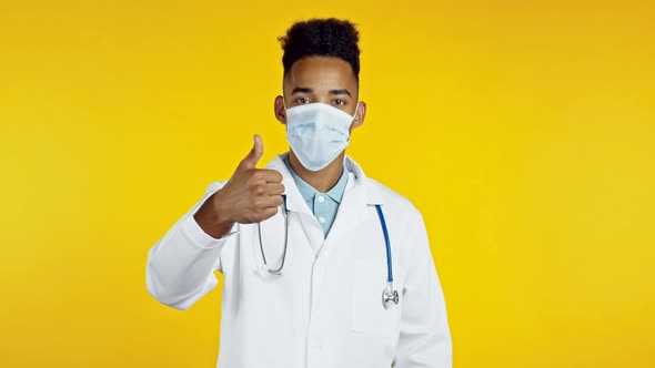 African American Man in Medical White Coat Showing Thumbs Up Sign Over Yellow Background. Positive